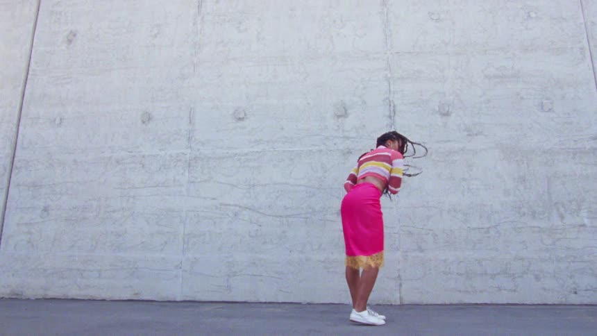 A young woman dances outdoors in front of a massive wall during the day