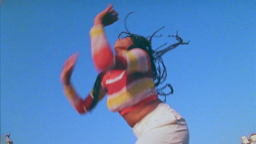 A young woman swinging her braids around and dancing outdoors at daytime