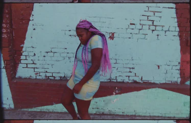 A teenage girl dances on a street in front of a brick wall