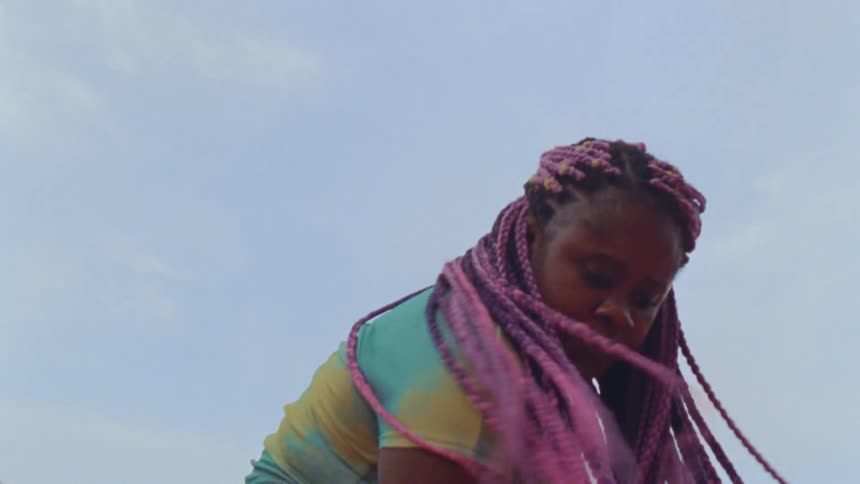 Young long haired woman energetically dancing in front of a clear blue sky