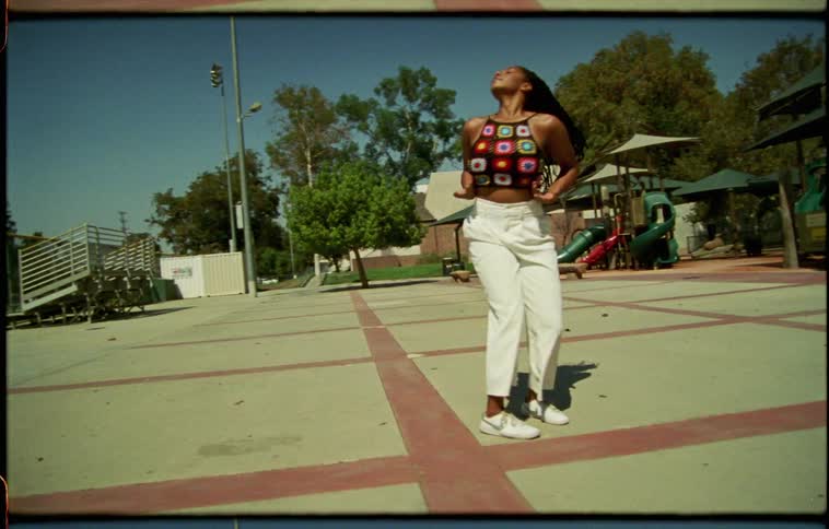 Woman dancing by herself in a park next to a playground and a baseball field at daytime