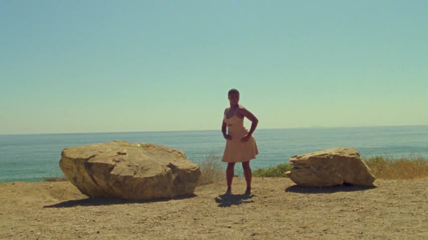 A young woman dancers on the coast near two large stones on a clear day