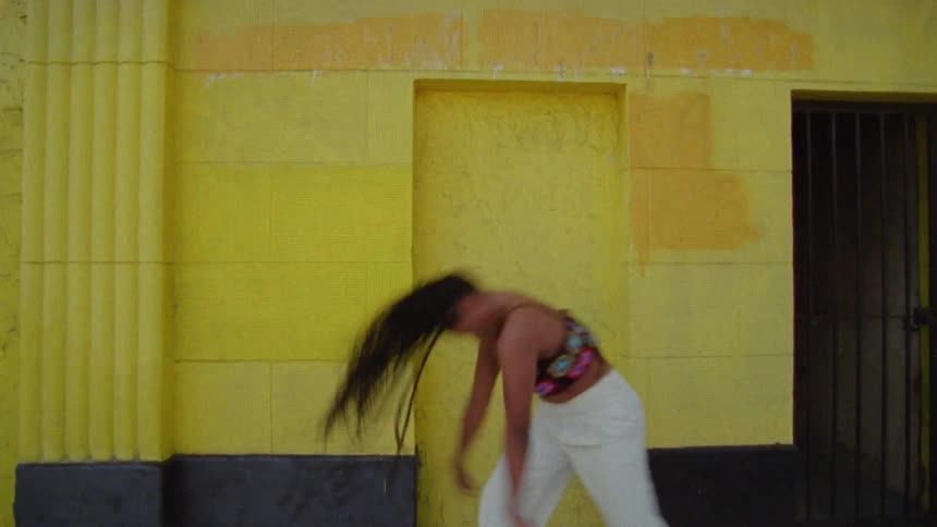 Young long haired woman dancing in front or a yellow wall