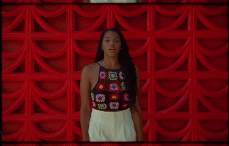 Young woman with long hair standing in front of a red wall looking at the camera