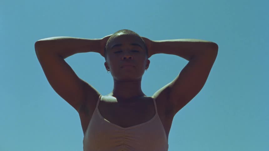 A woman standing with hands over her bald head looking at the camera