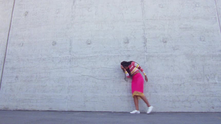 Young long haired woman energetically dancing in front a concrete wall