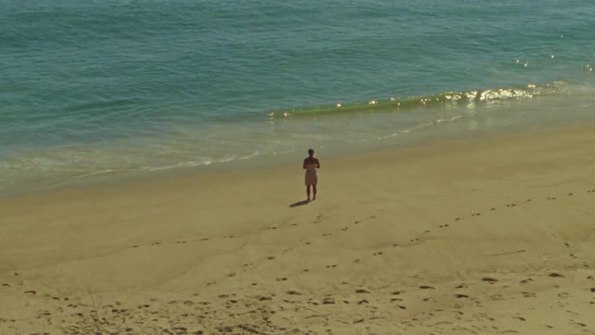 A woman stands on a yellow sand beach in front of the ocean tide coming in and out at daytime