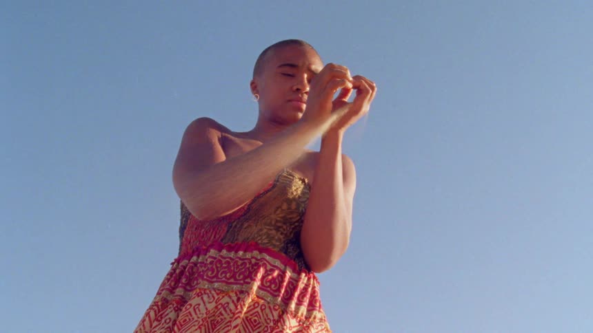 A teenage girl stands with her eyes closed as she lets sand run through her fingers