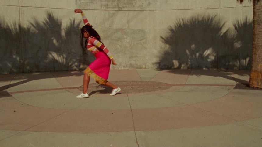 A woman dancing outside next to palm trees in a city at daytime