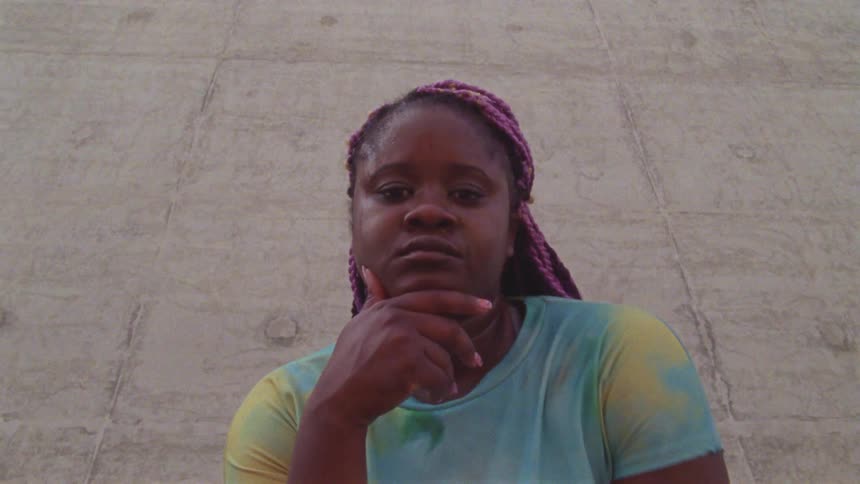 Woman reclined on a concrete wall walks into the camera