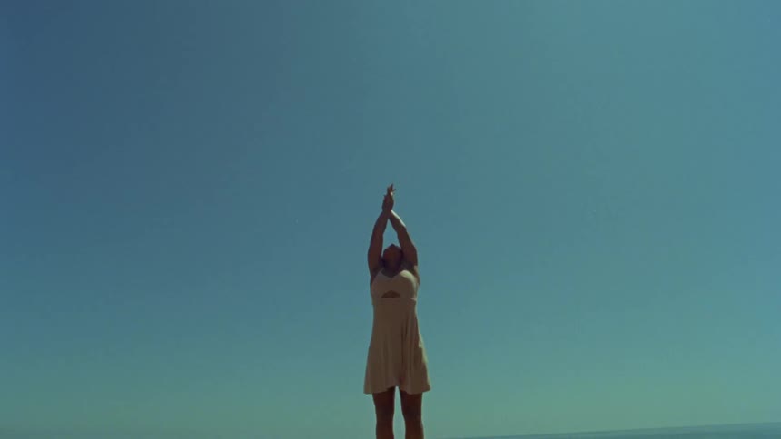 Woman standing outside putting her hands up into the air and performing a dance move with her hands at daytime