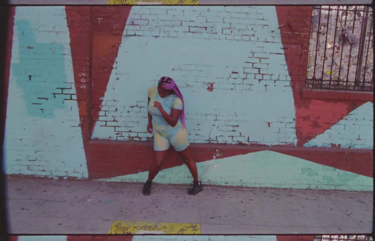 Woman dancing next to blue and red painted brick wall outdoors in an urban area at daytime