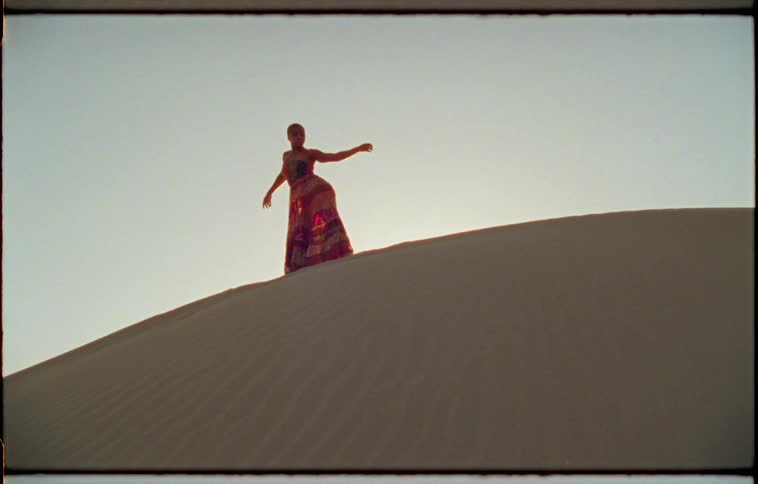 Woman dances on top of sand dune under clear blue sky