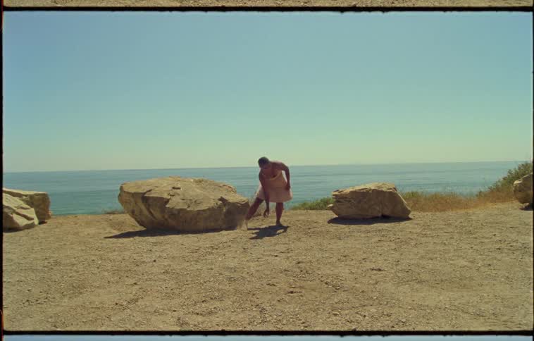 A woman performs a contemporary dance routine near large stones overlooking the ocean