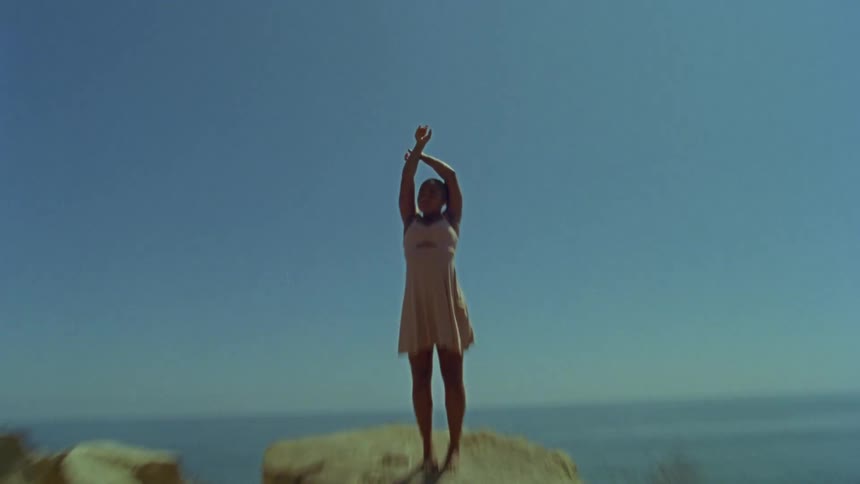 Woman wearing a pink dress standing on a rock near the ocean