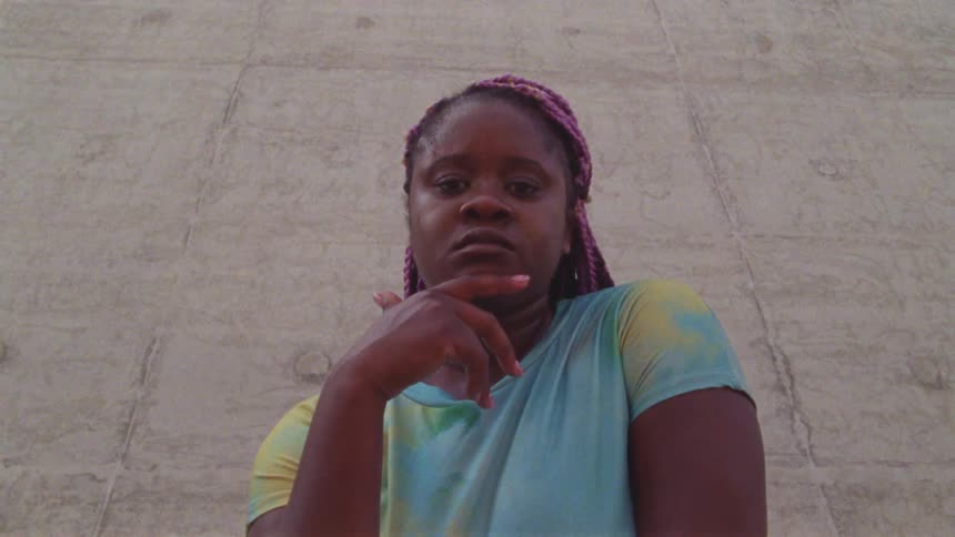 Woman walks up to a camera with a serious expression and makes a gesture with her hand