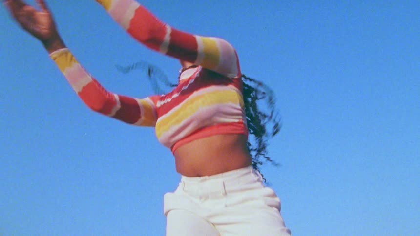 Young long haired woman energetically dancing in front of a clear blue sky