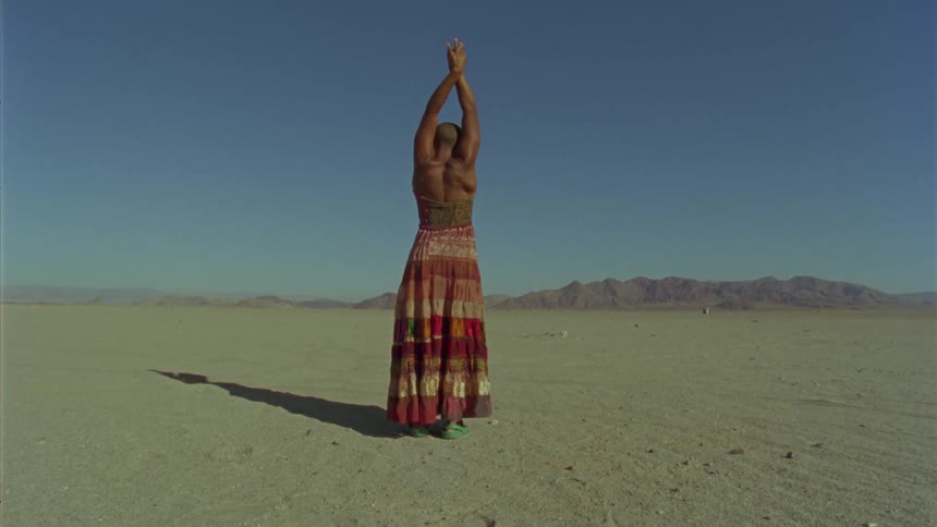 A woman stands in the desert and stretches her arms up above her head