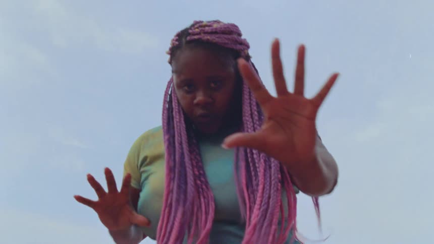 Young woman with long pink hair dances outdoors looking at the camera
