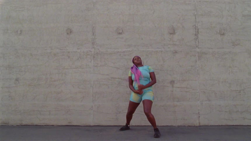 Young long haired woman energetically dancing in front a concrete wall surrounded