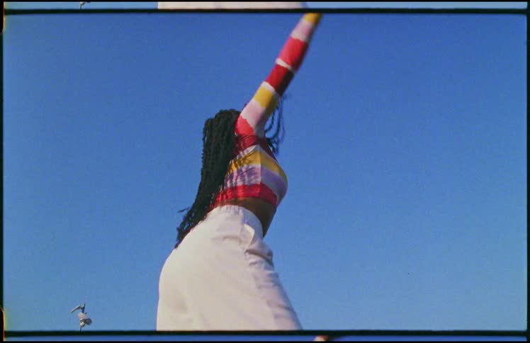 Young long haired woman energetically dancing in front of a clear blue sky