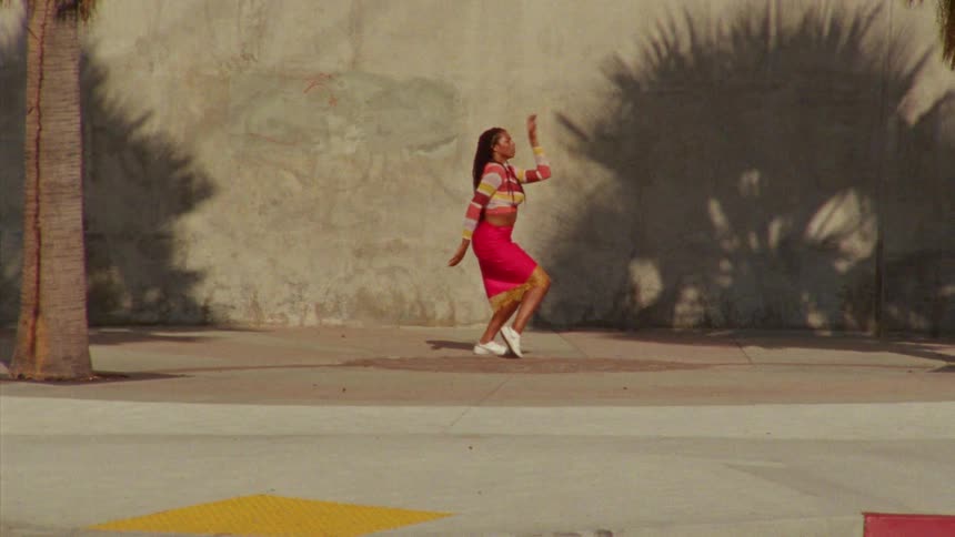 Young long haired woman energetically dancing in front a concrete wall surrounded by palm trees