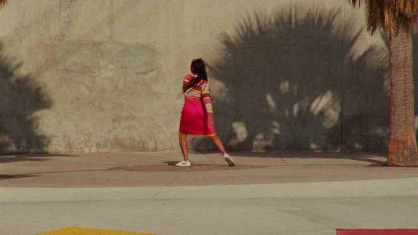 Young long haired woman energetically dancing in front a concrete wall surrounded by palm trees