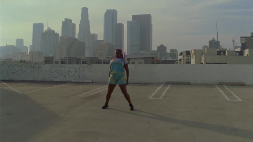 A woman on a rooftop dancing with buildings the sky and clouds in the background