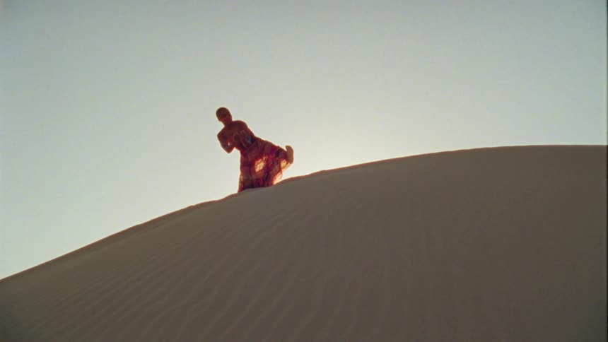 A woman dances on top a hill of sand in a desert at daytime