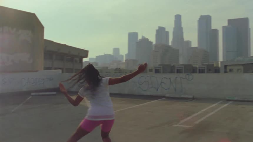 A young woman dances on the top floor of a parking lot in a metropolis during the day