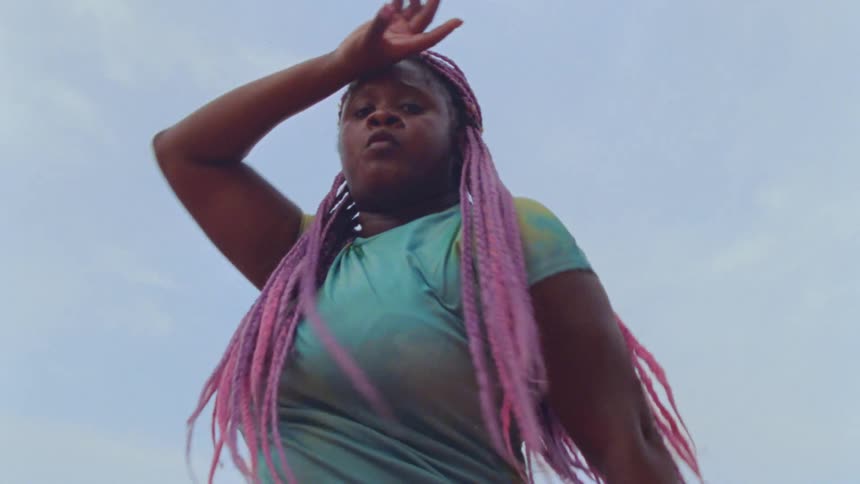 A woman with long pink braids dances outside
