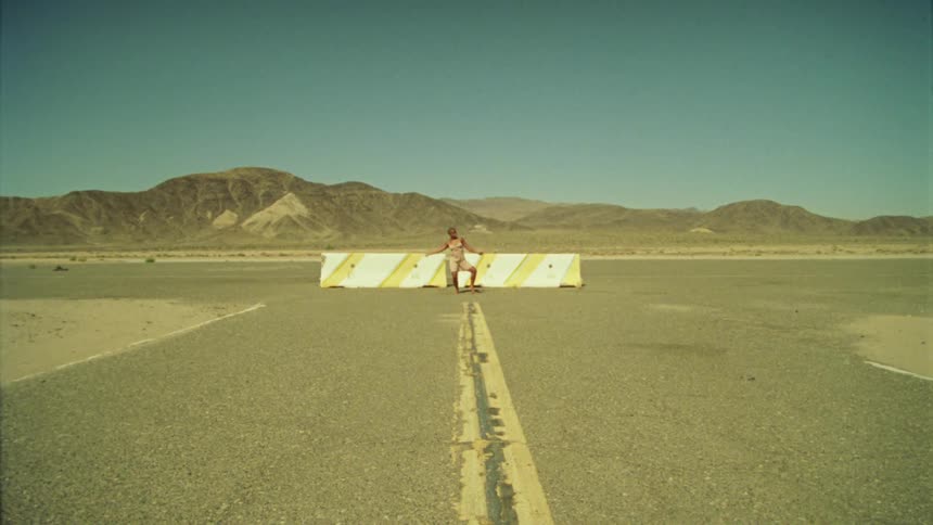 A man does a traditional dance in the middle of the road in front of a barrier near a desert canyon