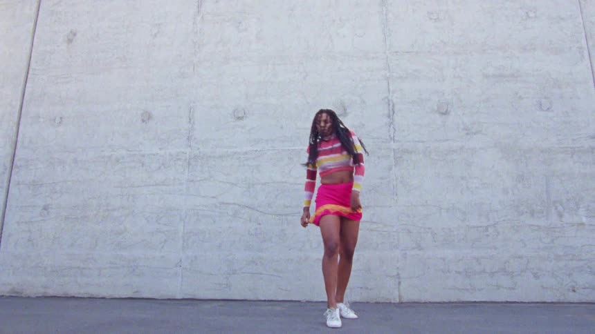 A woman with a sweater and skirt dancing in front of a wall