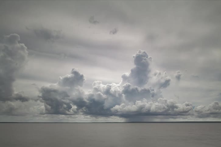 Cumulus clouds above an ocean move across the sky on a very cloudy day