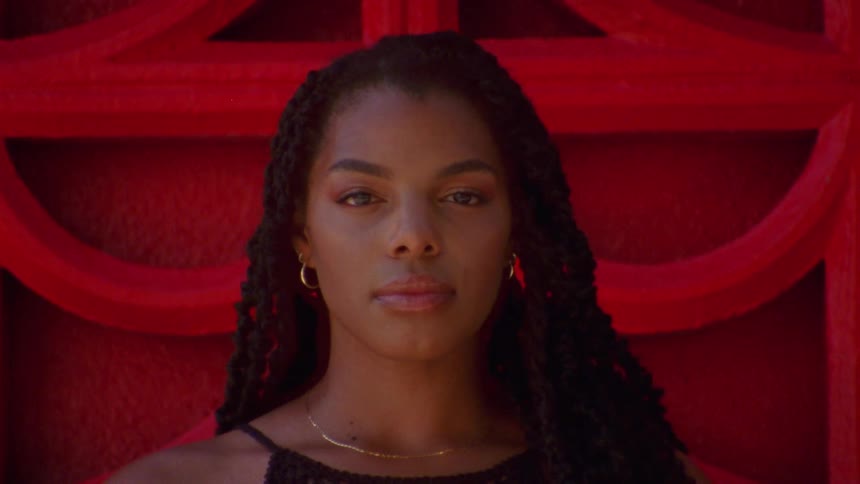 A young woman looks into the camera while standing in front of an elaborate red wall