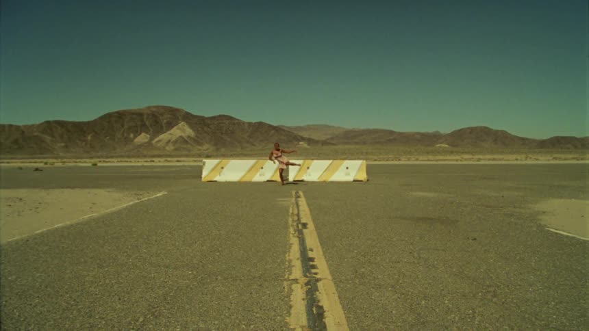 A woman dancing in a parking lot with a mountain range the sky and clouds in the background