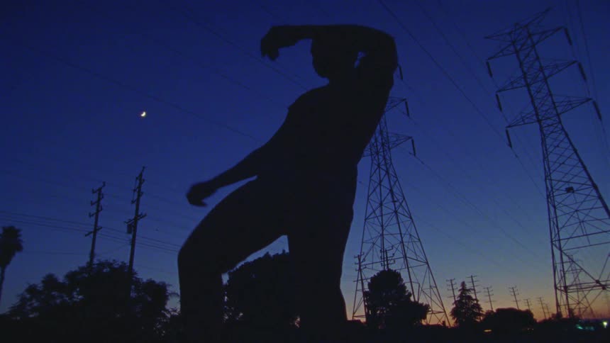 A woman energetically dancing near power lines and transmission towers under the full moon