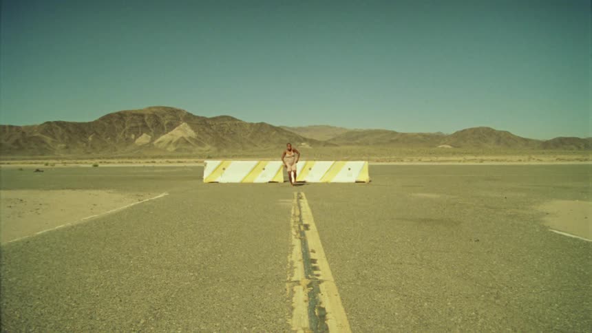 A woman dancing in a parking lot with a mountain range the sky and clouds in the background