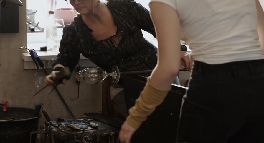 Two woman work together to form a glass goblet