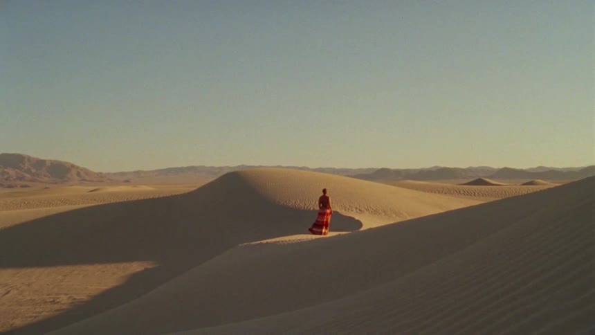 Woman in a red dress walking over the sand dunes on a desert