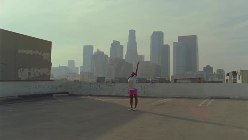 Woman dances in parking lot on roof of building with haze covered skyline in background