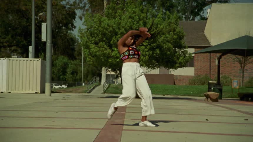 A young long haired woman kicking up while dancing on a public park
