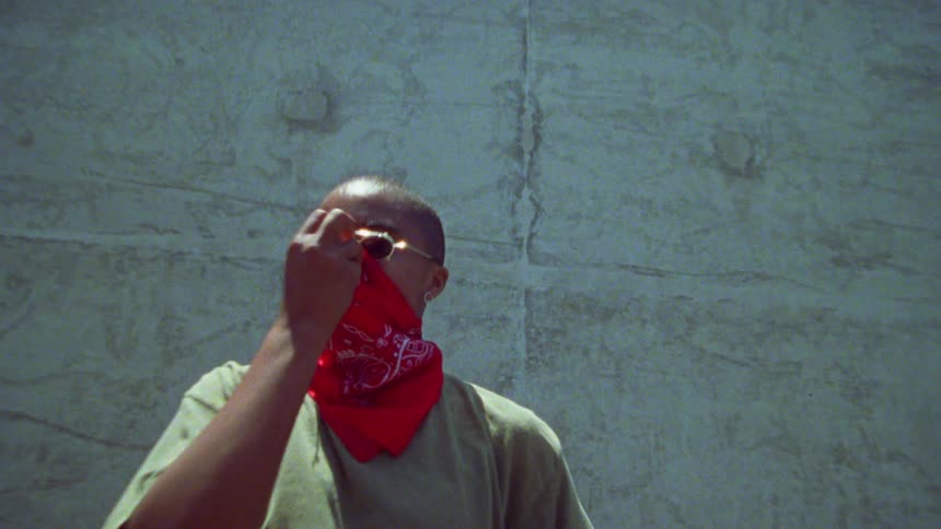 A woman standing by the wall lifts her bandanna over her face