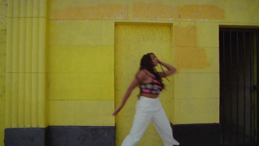 A young woman dances outdoors in front of a yellow building during the day