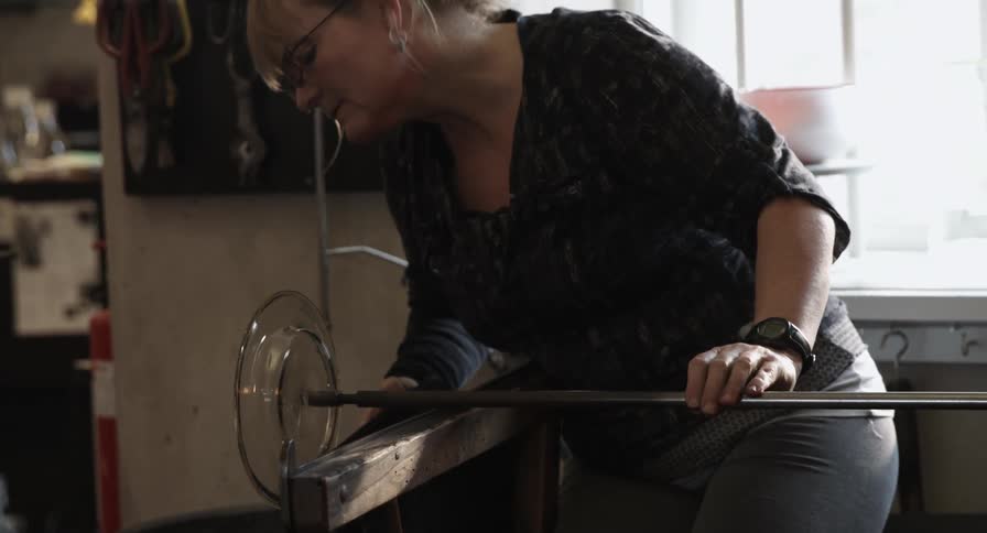 A woman is making a plate out of blown glass