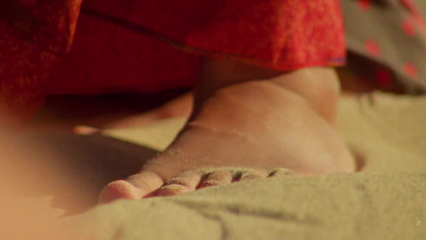 A barefoot woman moves her toes over the sand