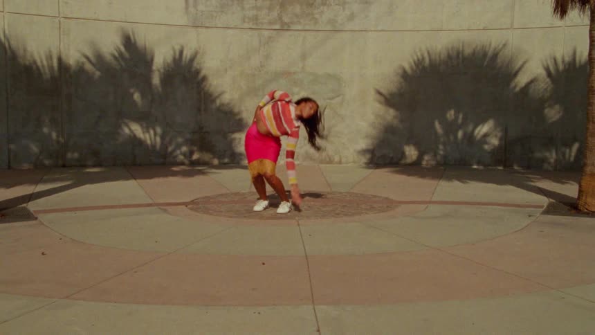 Young long haired woman energetically dancing in front a concrete wall surrounded by palm trees