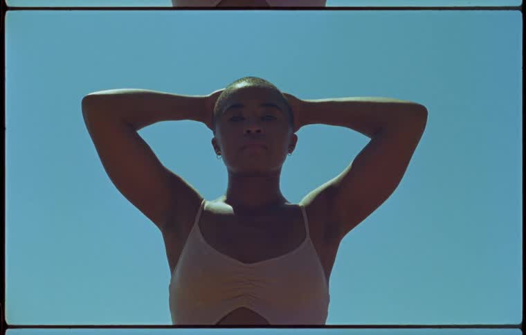 Bald woman standing with her hands on her head against a blue sky