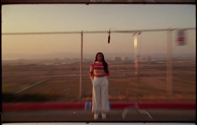 A woman is standing outdoors by a fence at dusk