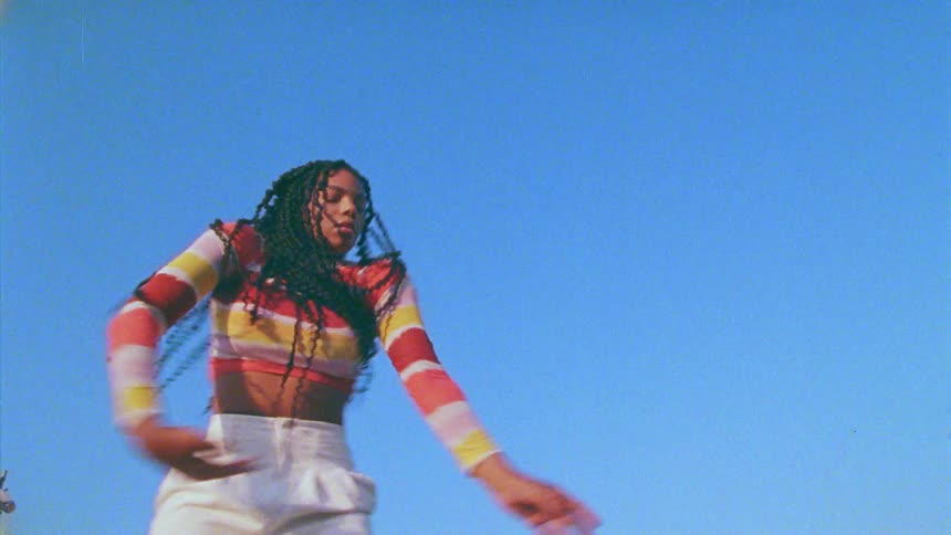 Woman with long braids dances under clear blue sky